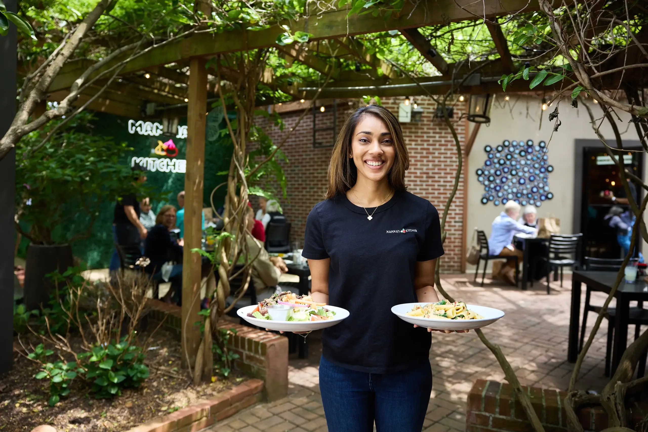 A Mamma’s Kitchen team member presents meals on the leafy patio.